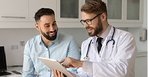 Médico mostra tablet a paciente sorridente em consultório.