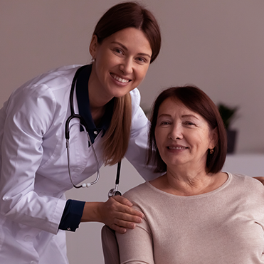 Médica ao lado de paciente idosa sorrindo durante atendimento.