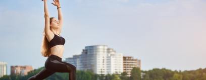 Mulher praticando exercício físico ao ar livre, com postura de alongamento em um parque urbano, representando a adoção de hábitos saudáveis e um estilo de vida ativo.